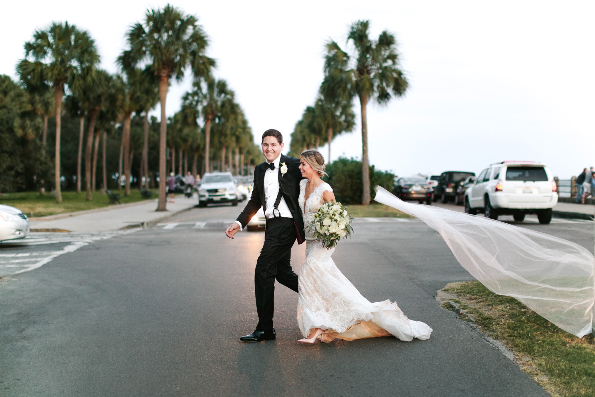 A joyful bride and groom cross the street unaware of the bride's veil flying in the wind. Moment captured by destination wedding photographer Rebecca Cerasani