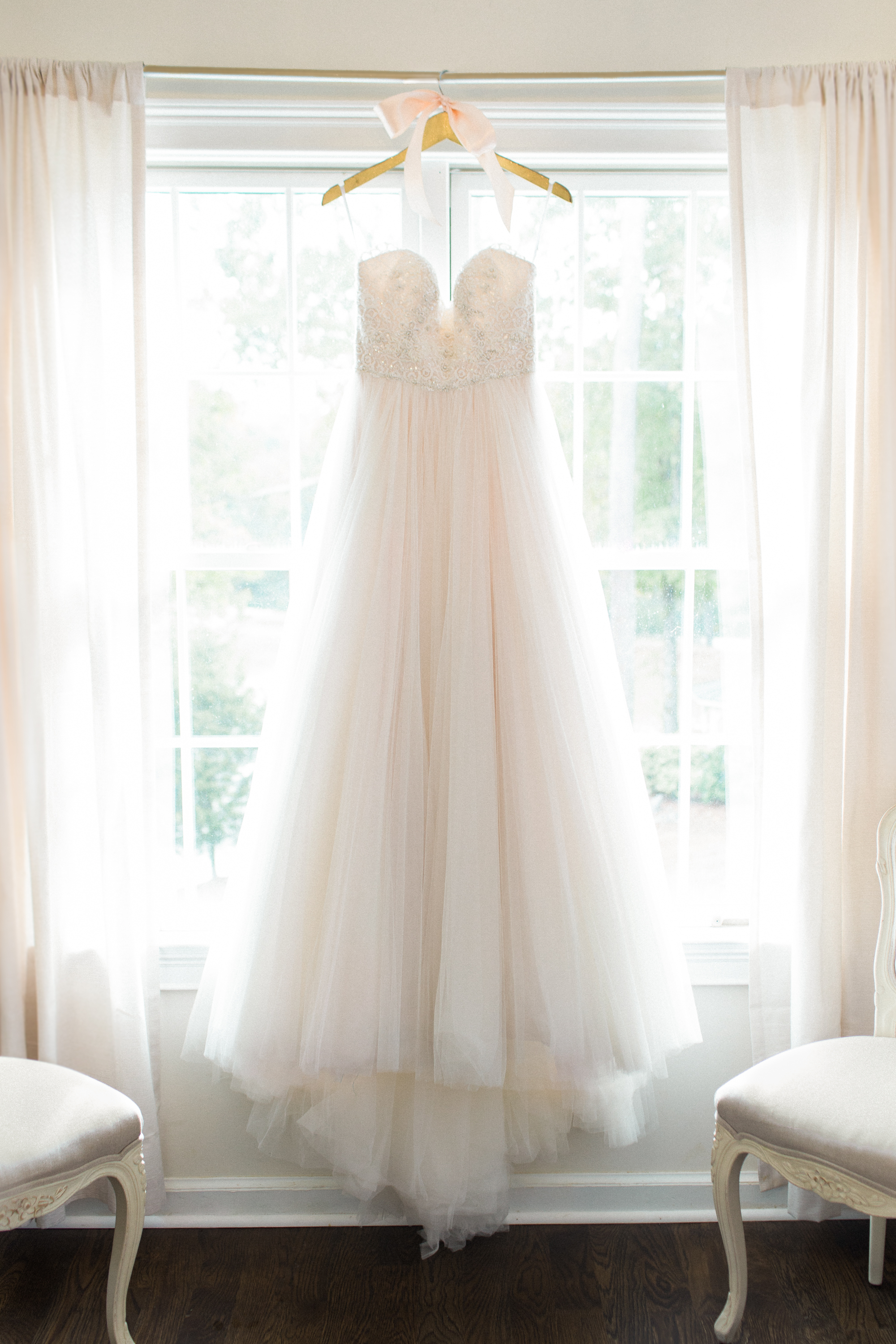 Beaded gown with tulle skirt hangs in window of Bridal Suite.