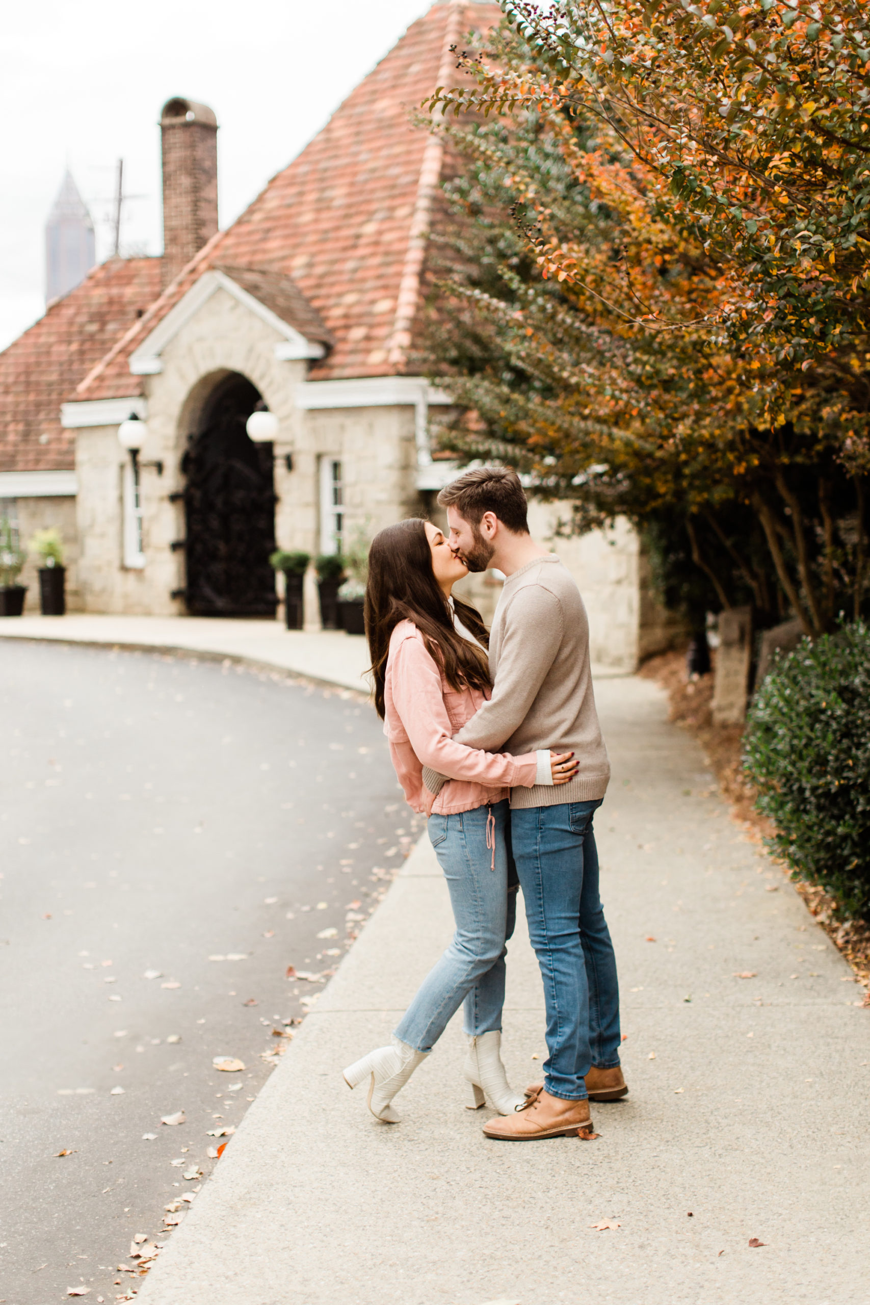 Engaged couple kiss on the sidewalk in front of Park Tavern near Piedmont Park